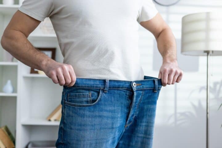 Person holding the waistband of loose-fitting jeans