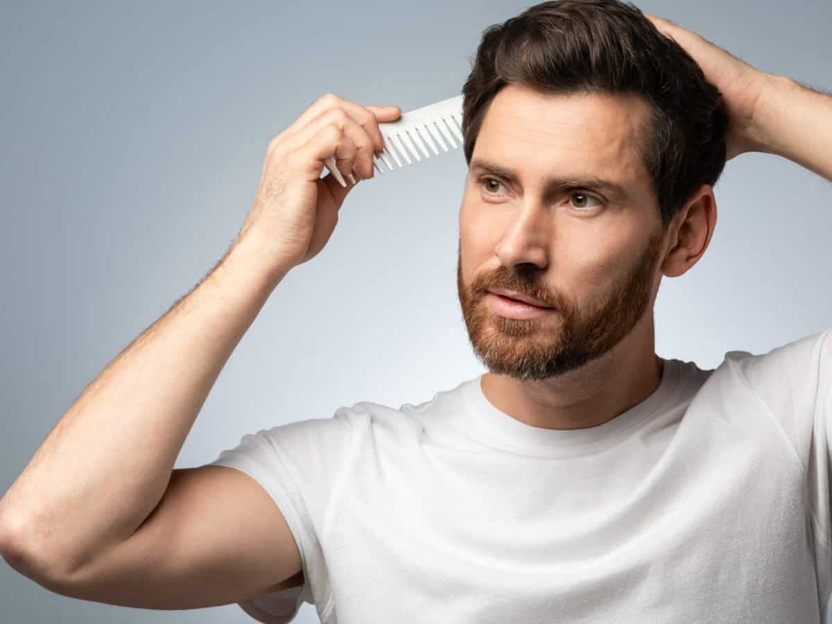 barber shop concept. handsome middle aged man in white t shirt brushing his hair, standing over grey studio background