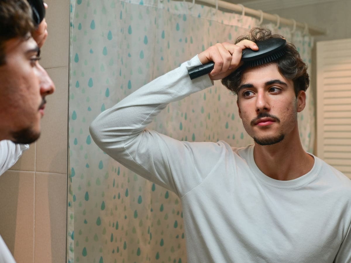 handsome man styling hair in bathroom mirror 2026 03 26 22 44 00 utc