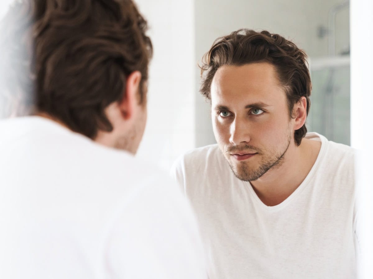 attractive young man standing in front of the bathroom mirror