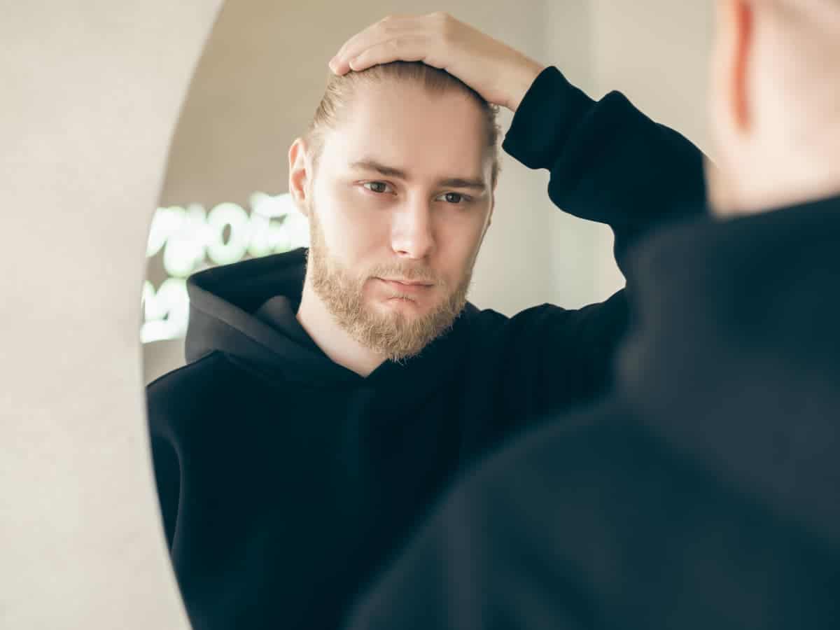 Hair Transplant Duration to Expect on the Day man with beard in hoodie looks in mirror 2026 03 24 04 42 26 utc