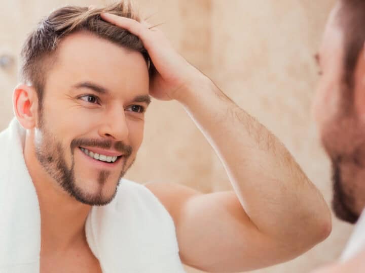 good morning to me. handsome young man touching his hair with hand and smiling while standing in front of the mirror