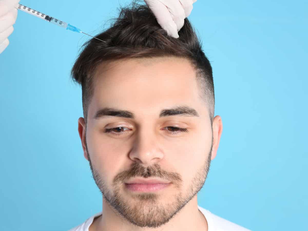 young man with hair loss problem receiving injection on color background